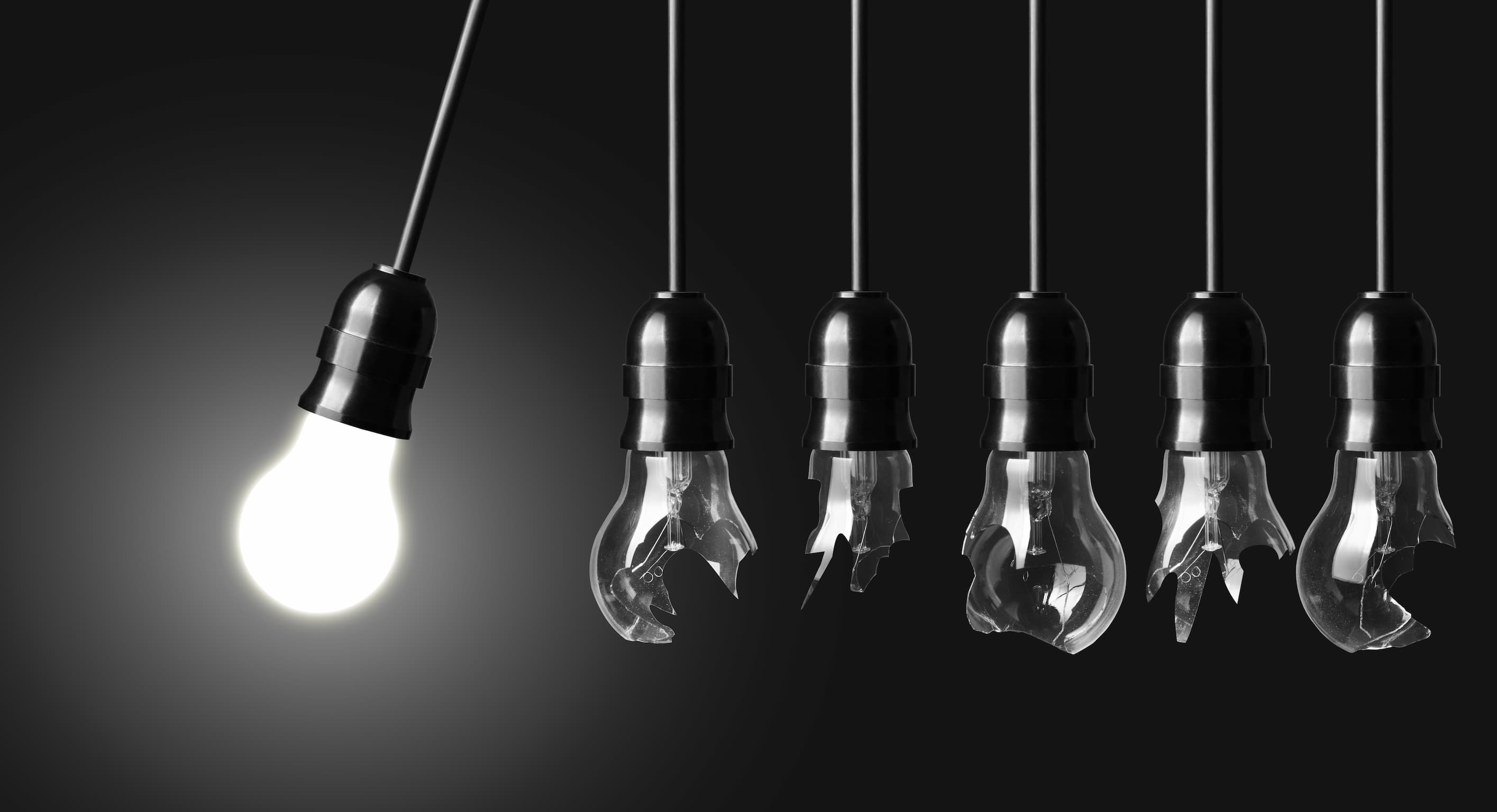 Section Image of hanging lightbulbs, the one farthest to the left is lit, but the others in line have all been broken by the momentum of the first bulb